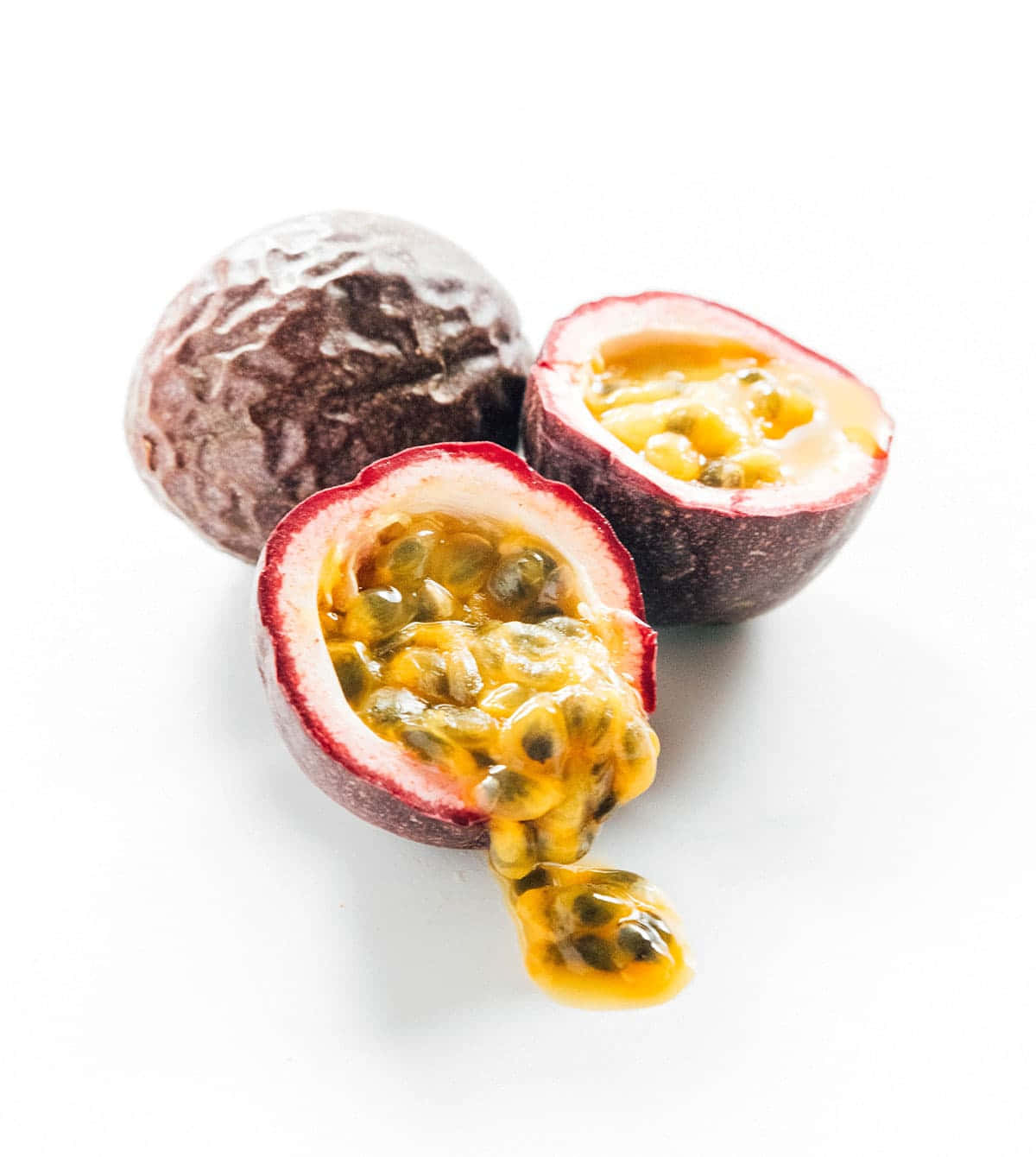 品嚐大自然的水果饗宴 壁紙 — 三個百香果，一個完整，一個切開，露出多汁的黃色果肉和黑色種子，放在乾淨的白色表面上。