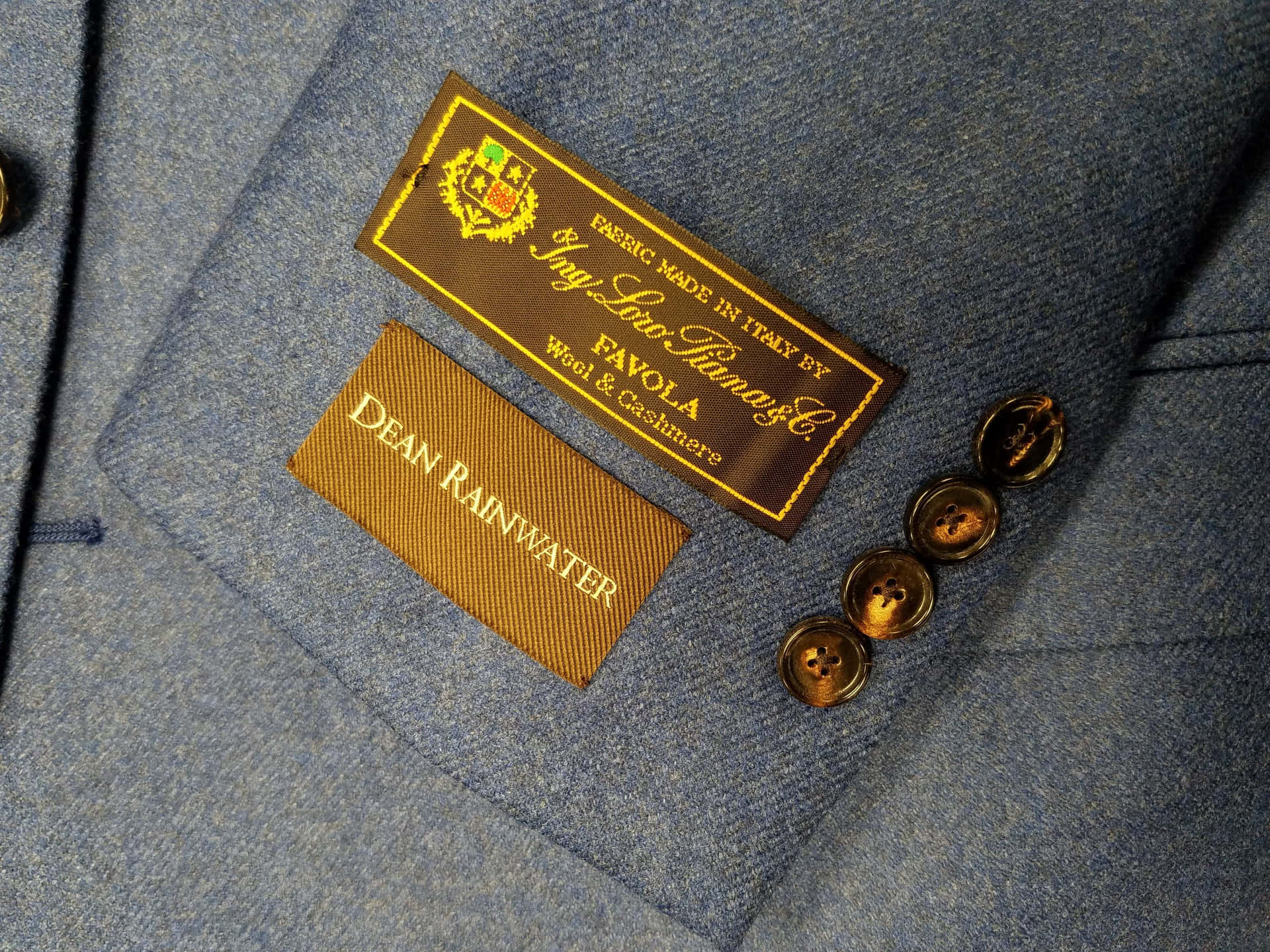 藍色西裝外套近距離特寫，帶有品牌標籤和金色鈕扣。