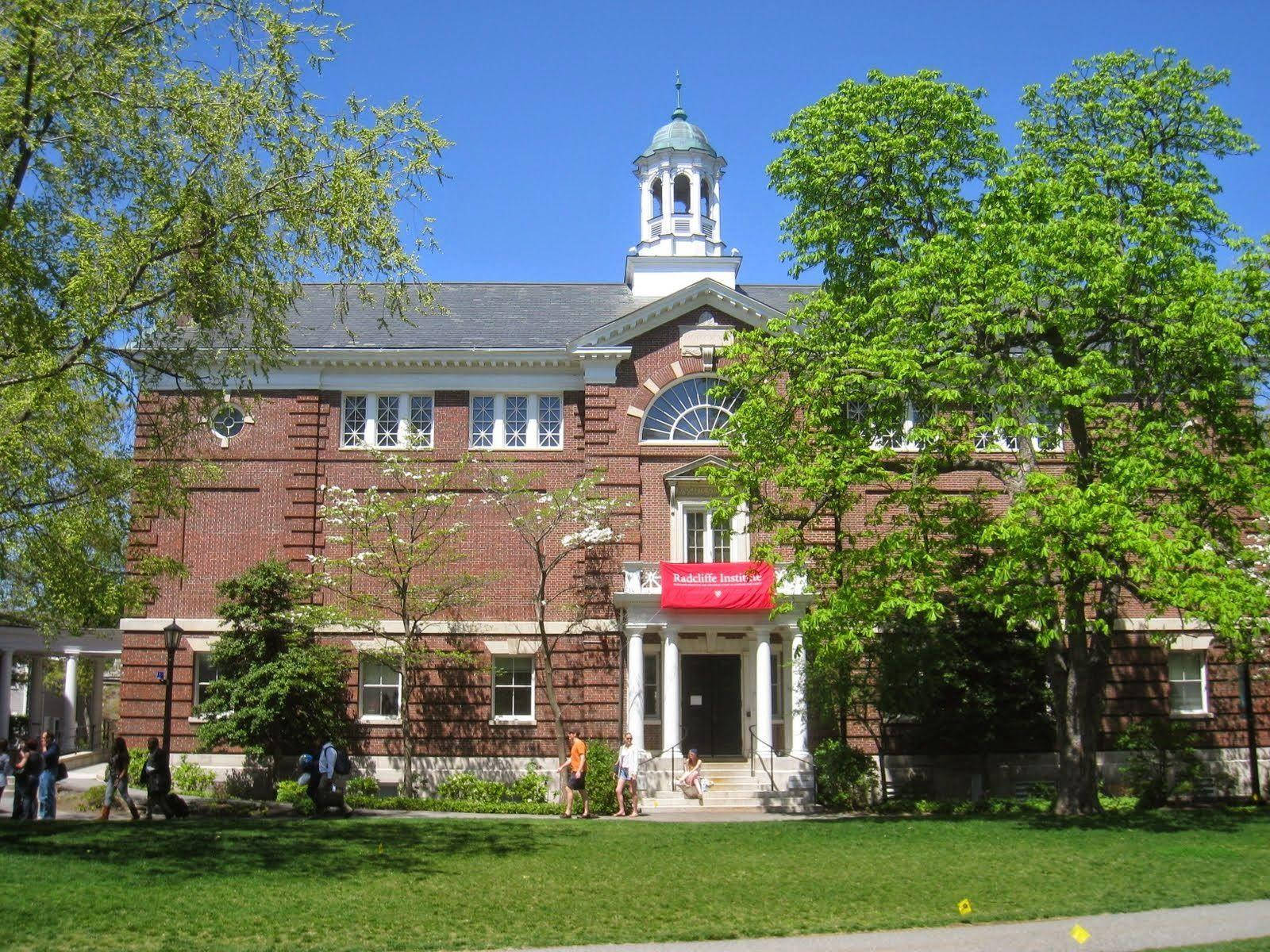 學生們走近一座帶有鐘樓和綠樹的歷史磚造大學建築。