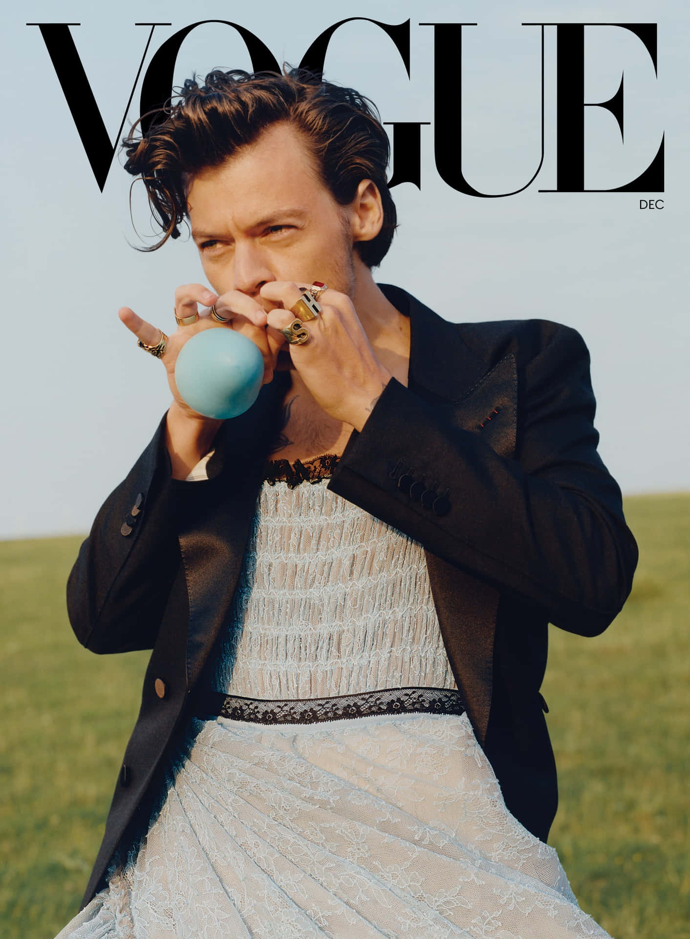 Harry Styles 在田野中穿著黑色西裝外套和白色連衣裙吹出藍色泡泡糖泡泡。