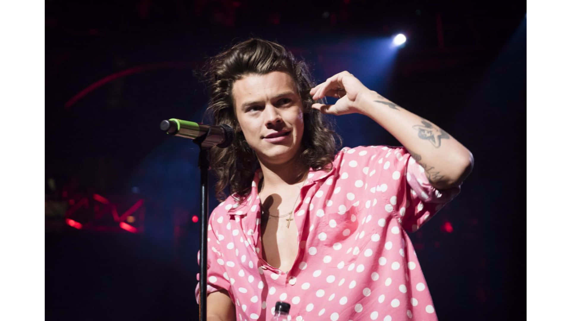 Harry Styles 穿著粉紅色圓點襯衫在舞台上唱歌。