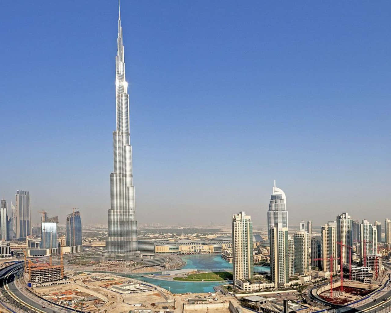 Burj Khalifa 桌布 壁紙 — 哈利法塔在晴朗的藍天下聳立於杜拜的天際線，周圍環繞著現代摩天大樓和建築工地。