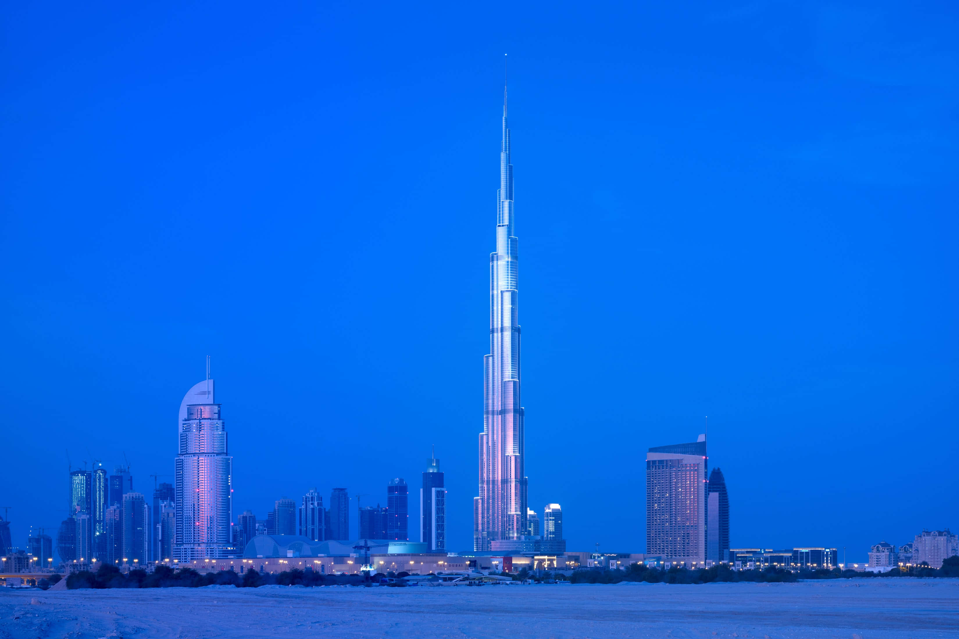 Burj Khalifa 桌布 壁紙 — 哈利法塔在暮色中聳立於杜拜天際線之上，深藍色的天空和閃爍的城市燈光倒映在水面上。