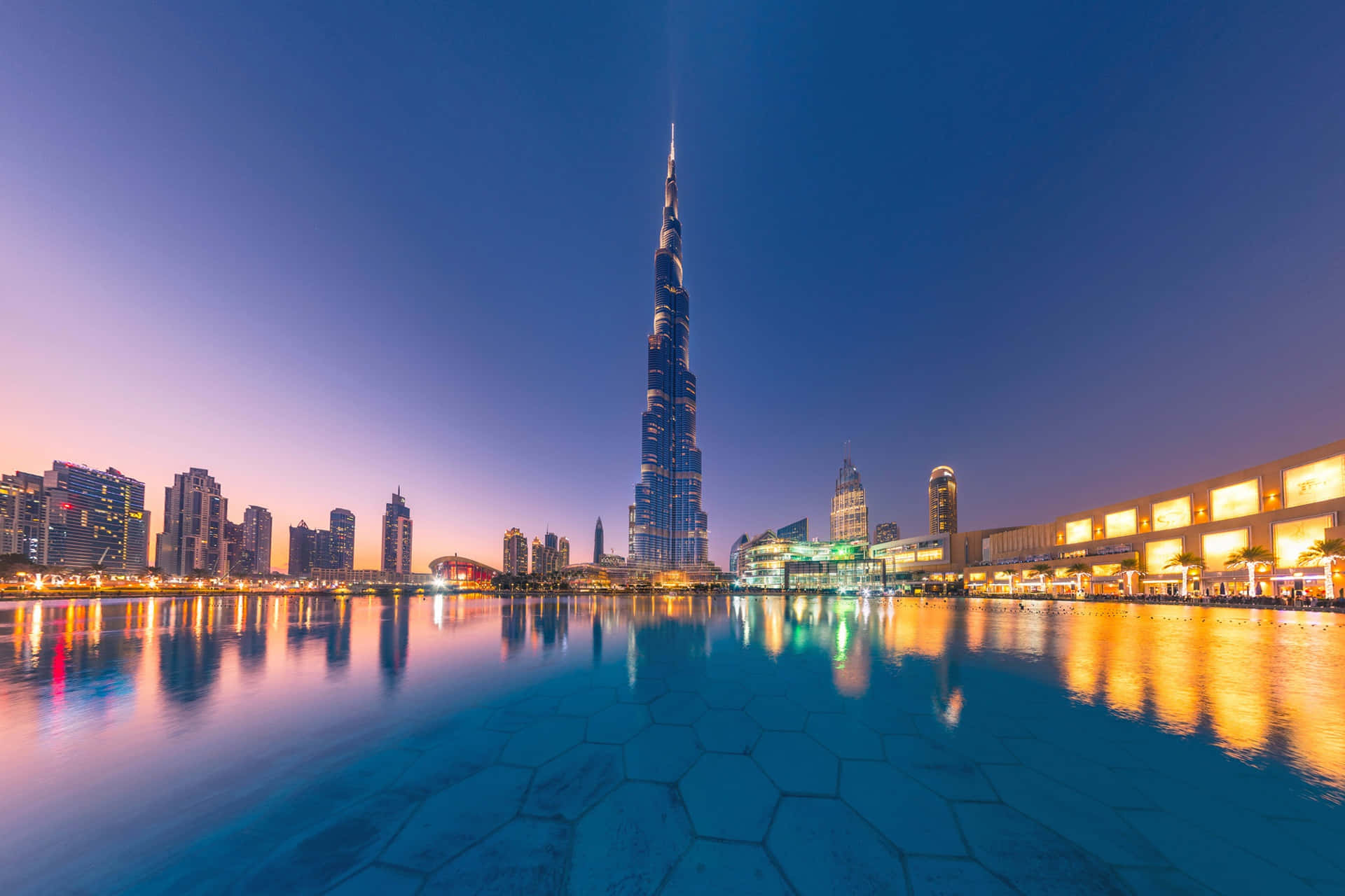 Burj Khalifa 桌布 壁紙 — 哈利法塔在暮色中聳立於杜拜天際線之上，其燈光倒映在下方平靜的水池中。