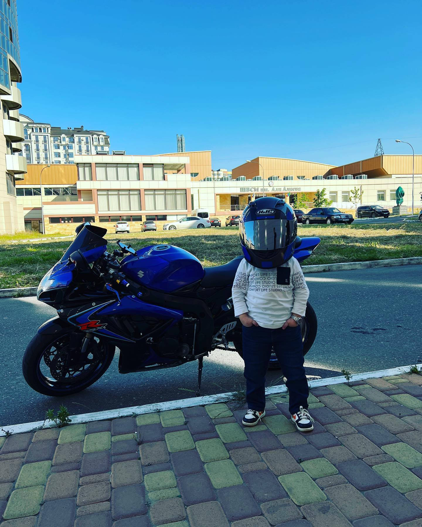 戴頭盔的孩子站在藍色摩托車旁邊的人行道上。