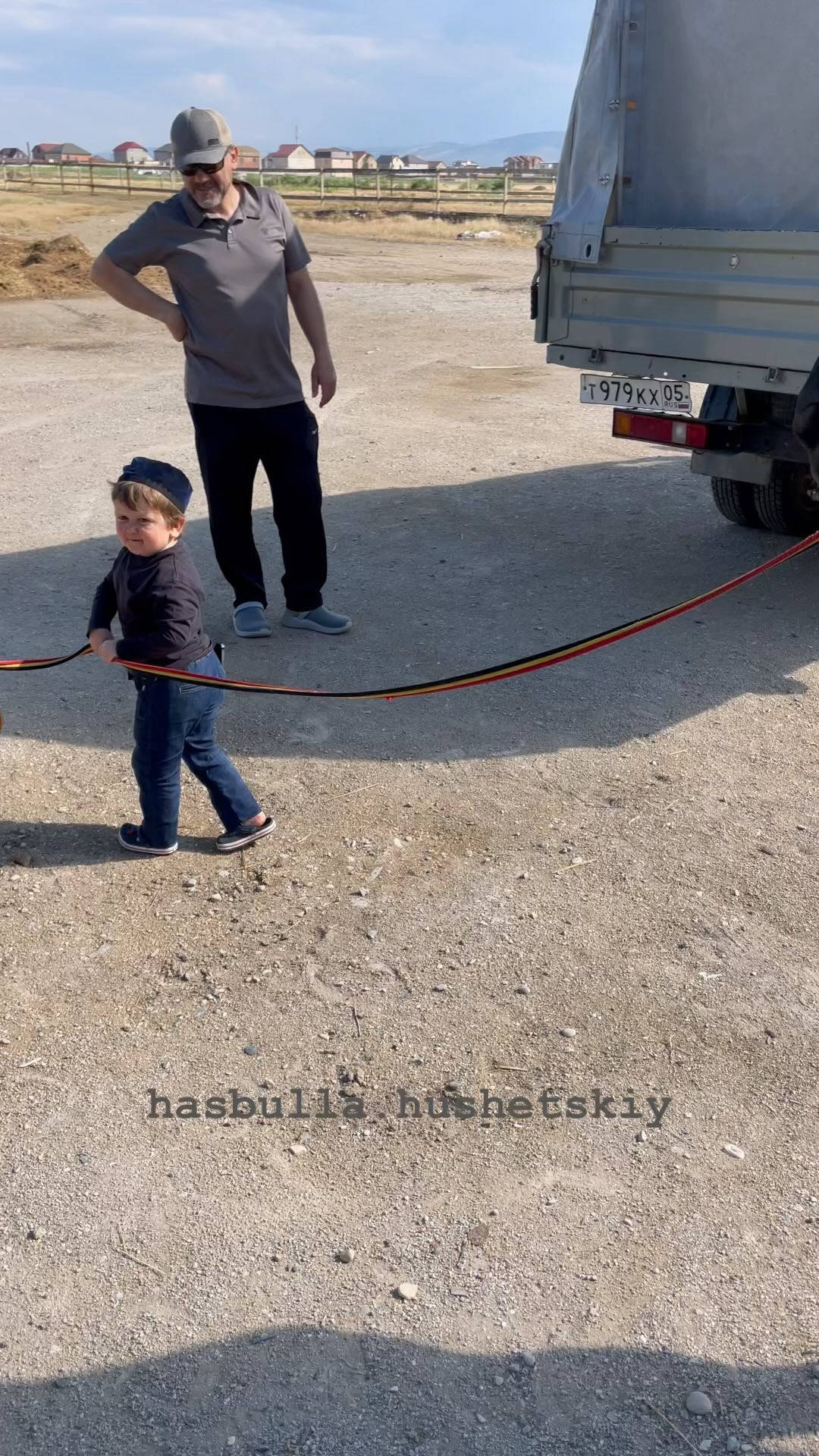 一名男子和一個幼兒站在碎石上的卡車附近，他們之間有一條繩子。