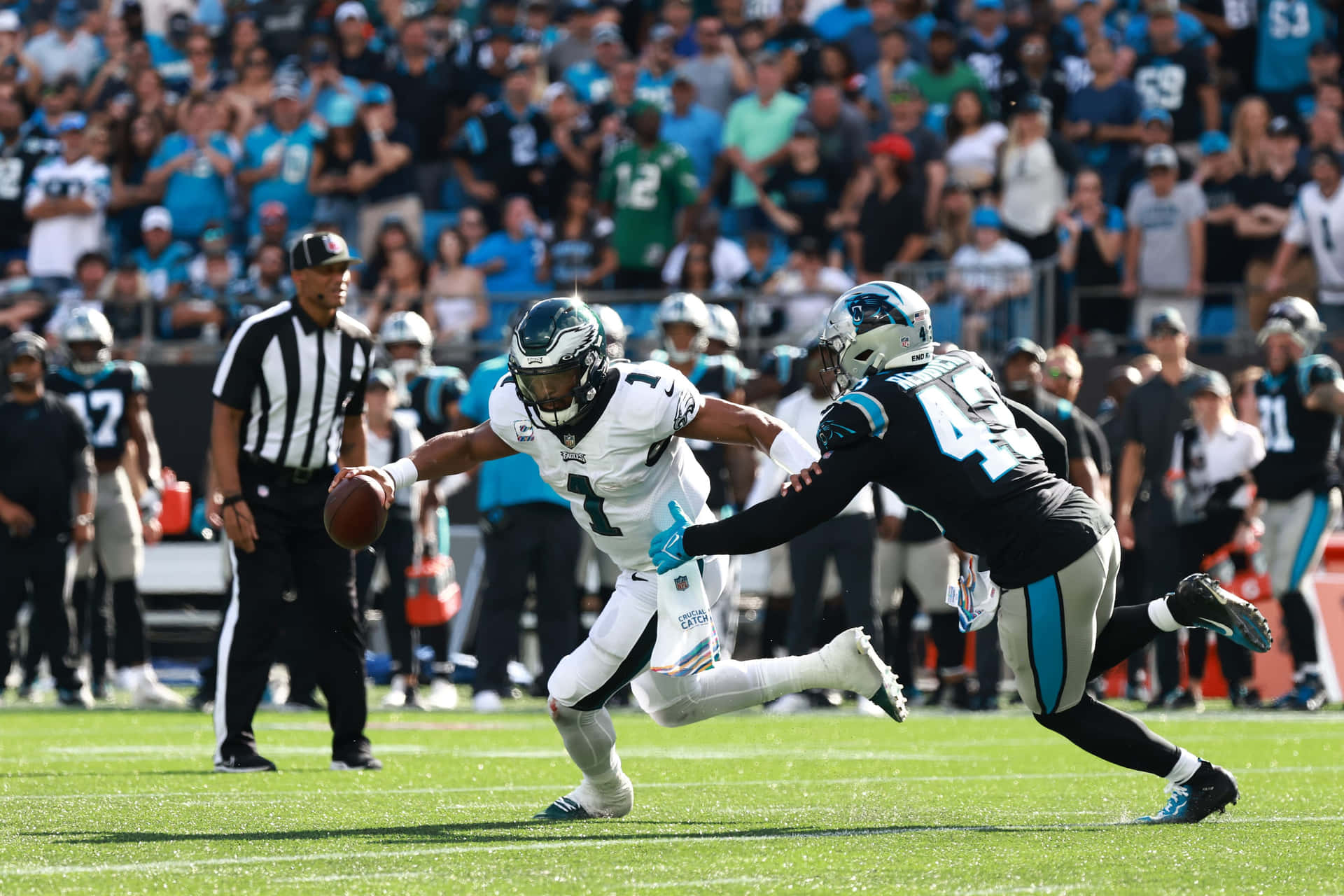 NFL四分衛在日間比賽中躲避防守球員，背景有觀眾。