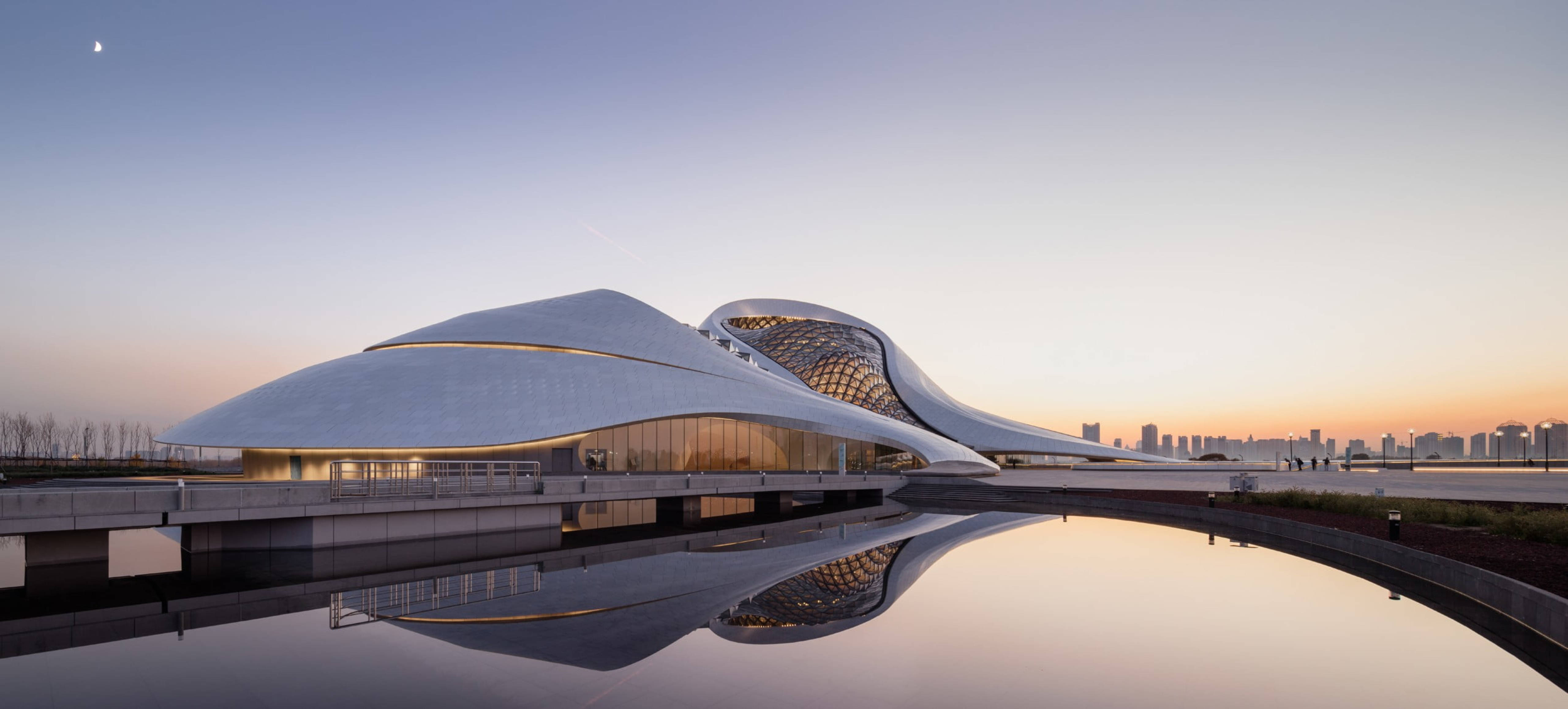哈爾濱大劇院建築風景 壁紙 — 一座未來主義的白色建築奇蹟，流暢的曲線在暮色中完美倒映在平靜的水面上。