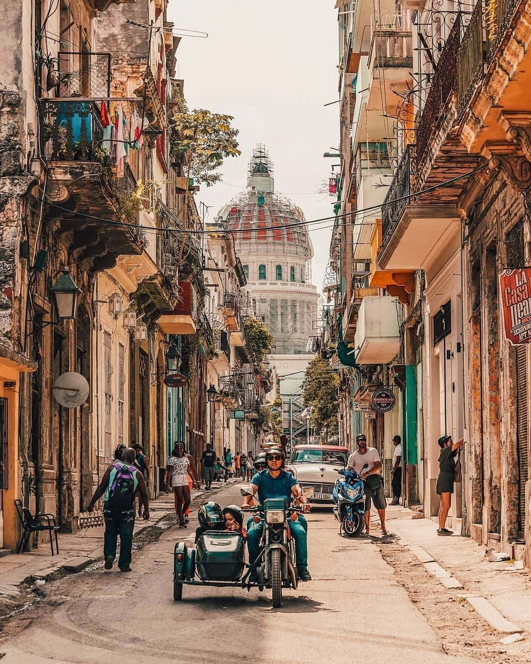 Cuba 桌布 壁紙 — 哈瓦那充滿活力的街景，一輛機動三輪車駛過殖民時期建築物和遠處的國會大廈圓頂。