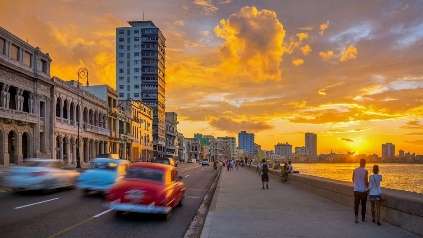 Cuba 桌布 壁紙 — 哈瓦那海濱的 vibrant 日落，經典汽車在歷史建築旁飛馳而過，行人沿著海濱長廊漫步。