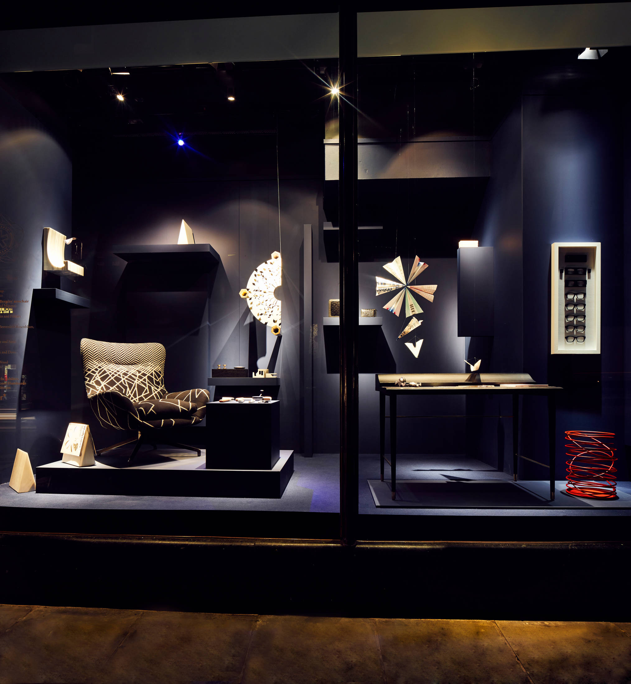 哈羅德百貨窗櫥展示的家具 壁紙 — 時尚現代家具店櫥窗展示，配有圖案椅子、幾何雕塑和黑暗牆壁上的發光燈光。