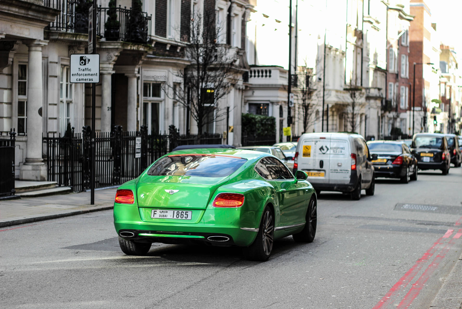 哈羅德百貨綠色汽車經過 壁紙 — 一輛充滿活力的綠色賓利 Continental GT 沿著倫敦綠樹成蔭的街道行駛，經過經典的聯排別墅和交通攝像頭。