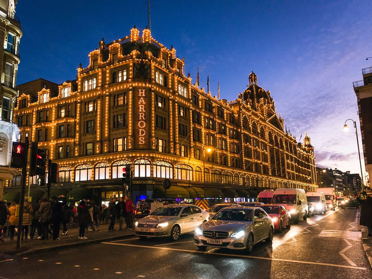 哈羅德百貨藍天下的美景 壁紙 — Harrods 百貨公司在暮色天空下溫暖地發光，汽車和行人沿著潮濕的城市街道移動。