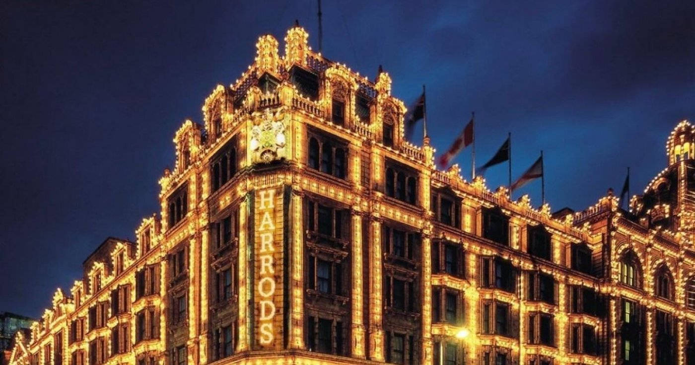 哈羅德百貨黃色燈光 壁紙 — Harrods 百貨公司在深藍色的夜空下溫暖地發光，精緻的金色燈光勾勒出其宏偉的建築輪廓。