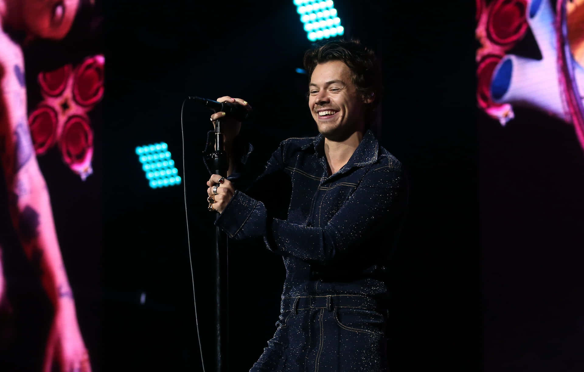 Harry Styles 喺表演期間喺舞台上微笑揸住咪高峰。