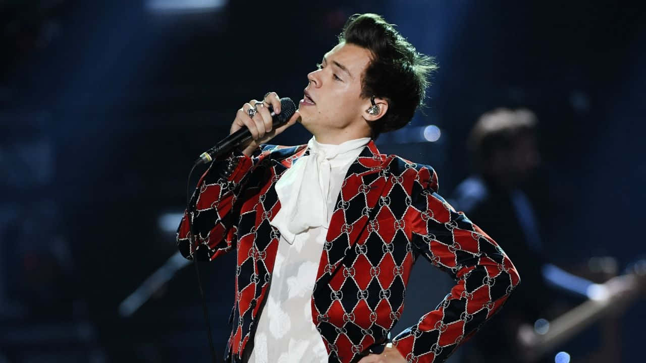 Harry Styles 穿著紅黑圖案外套在舞台上表演。