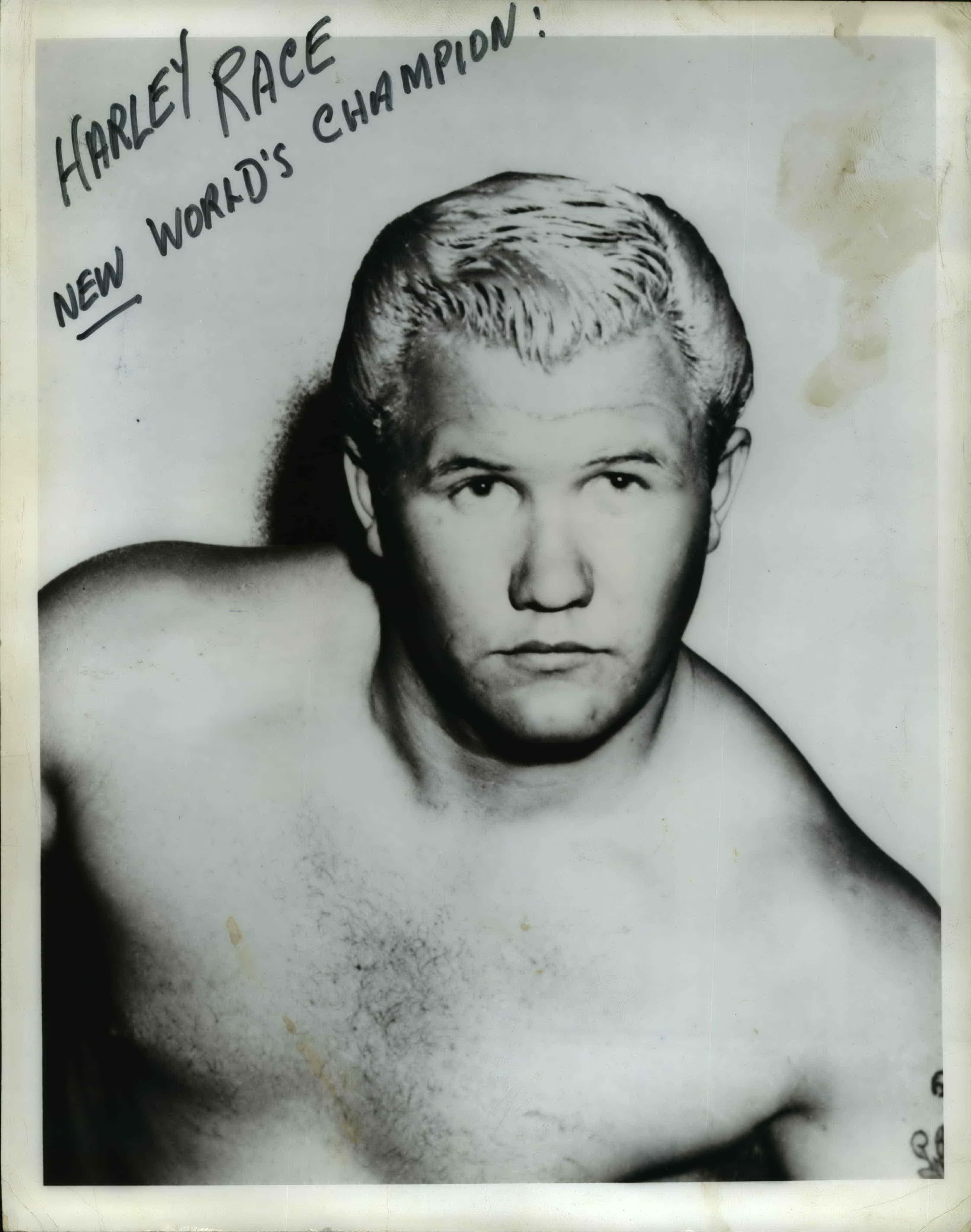 哈雷·雷斯經典舊照 壁紙 — 一張摔角手 Harley Race 的復古黑白肖像照，照片上手寫文字宣佈他為「New World's Champion」。