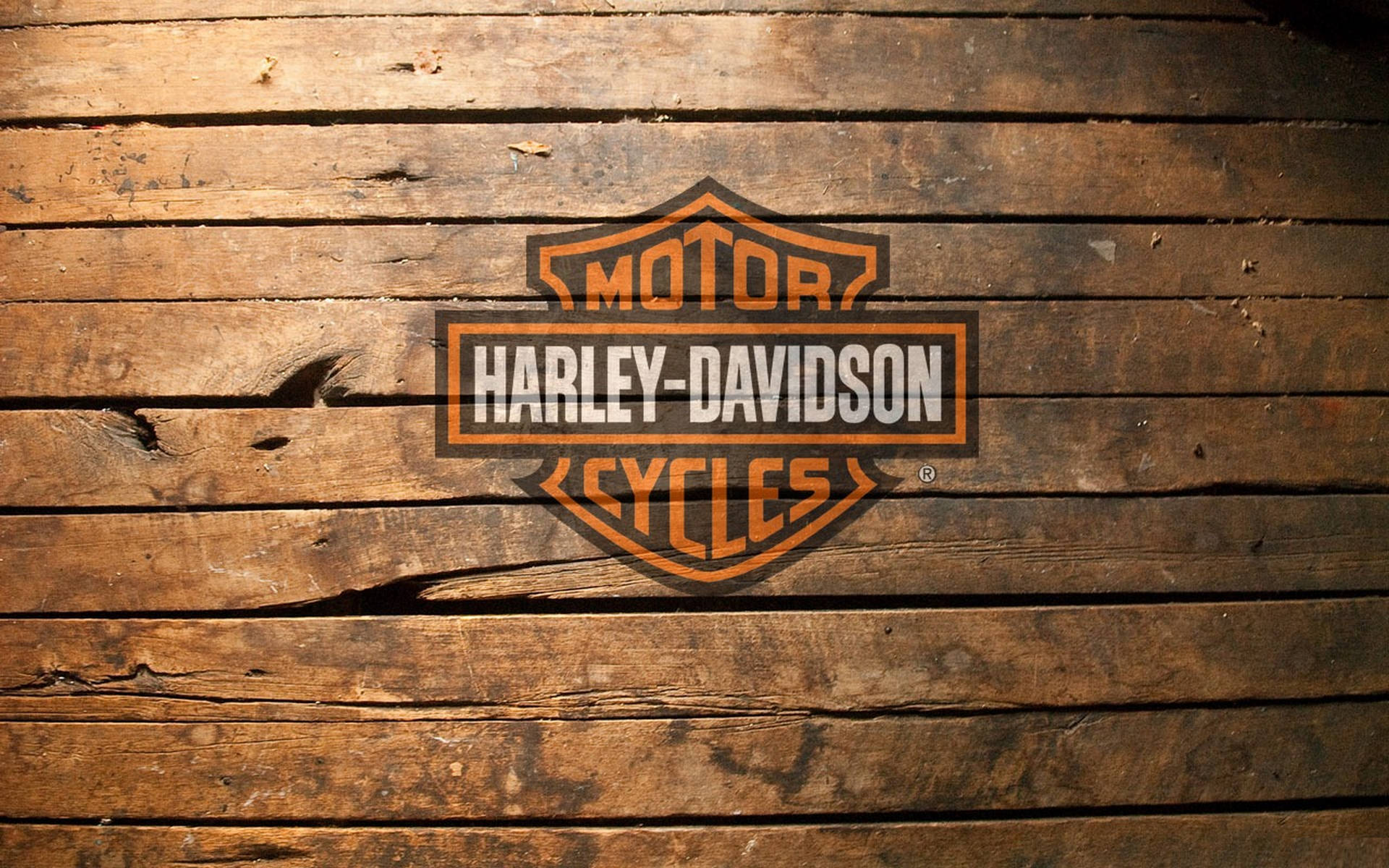 哈雷戴維森標誌木紋背景 壁紙 — 橙色和黑色的Harley-Davidson標誌放置在風化的木板上，木紋和裂縫清晰可見。