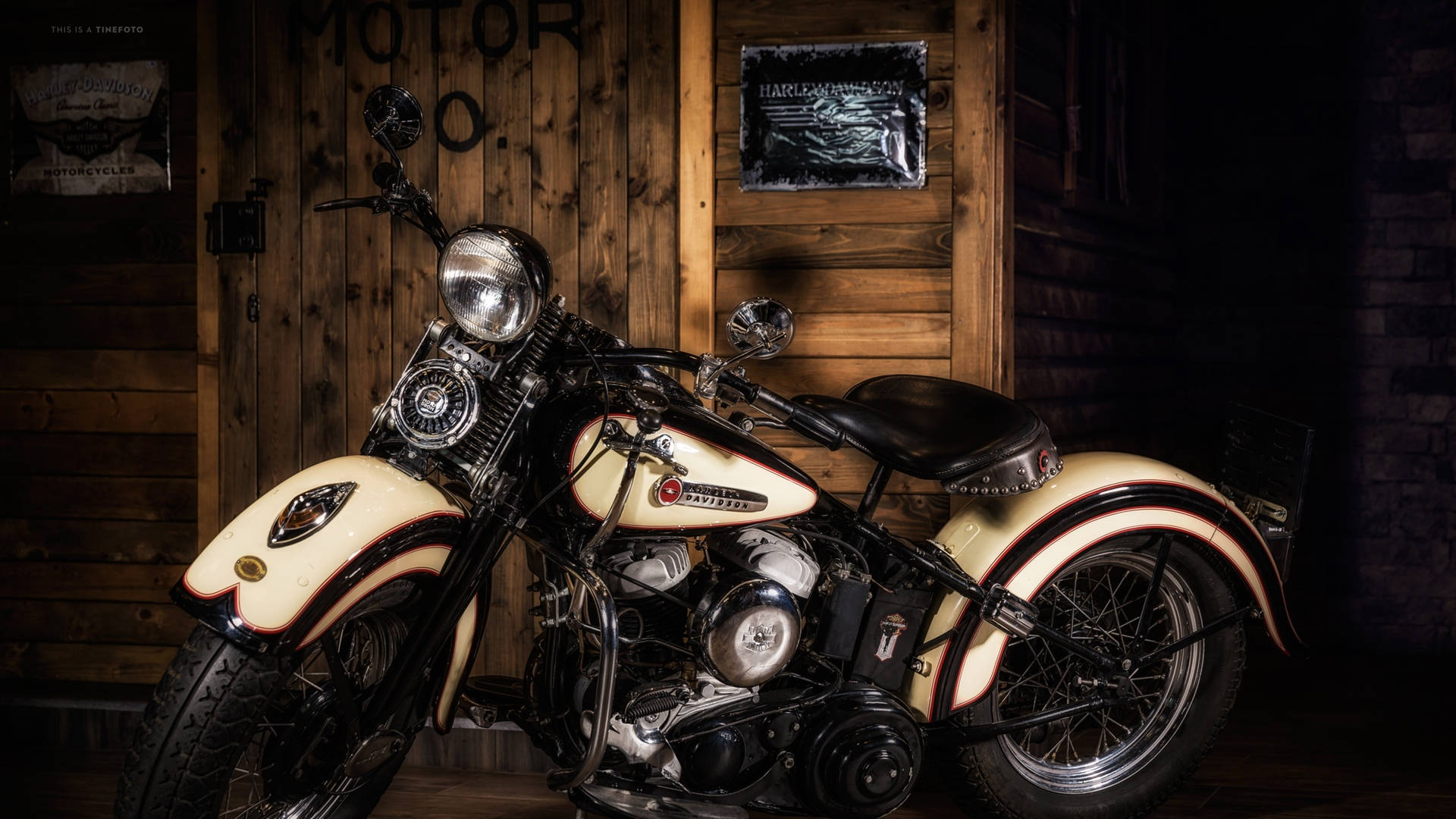哈雷戴維森標誌經典摩托車 壁紙 — 一輛復古奶油色和黑色的Harley-Davidson電單車在溫暖燈光下於質樸的木車庫中閃閃發光。