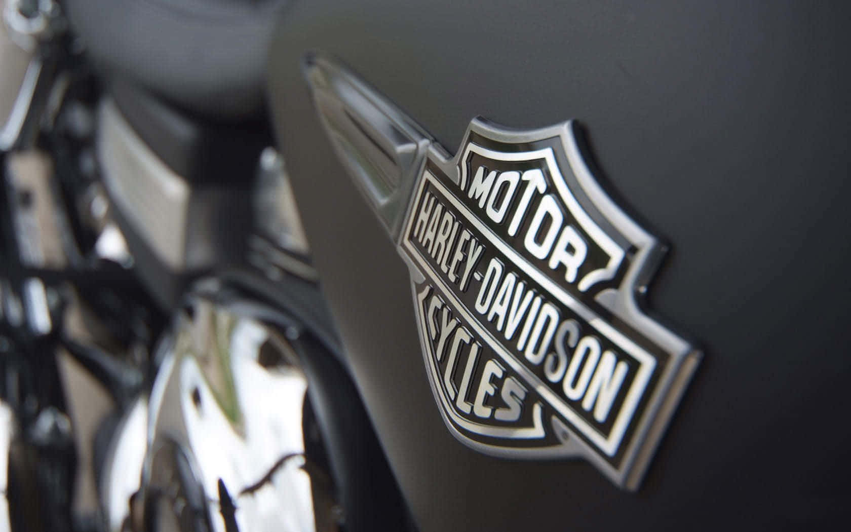 啞光黑色電單車油缸上嘅鍍鉻Harley-Davidson標誌，引擎模糊。
