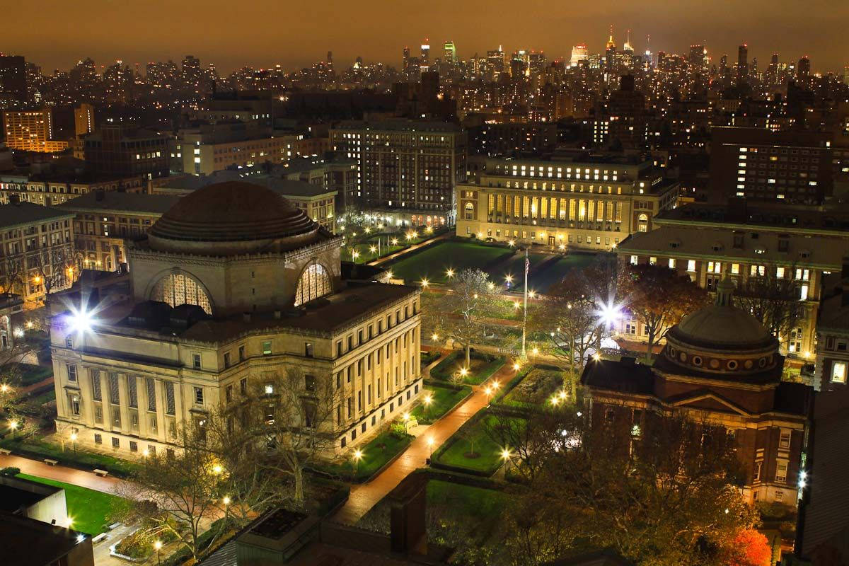 大學校園的夜景，建築物燈火通明，背景是城市天際線。