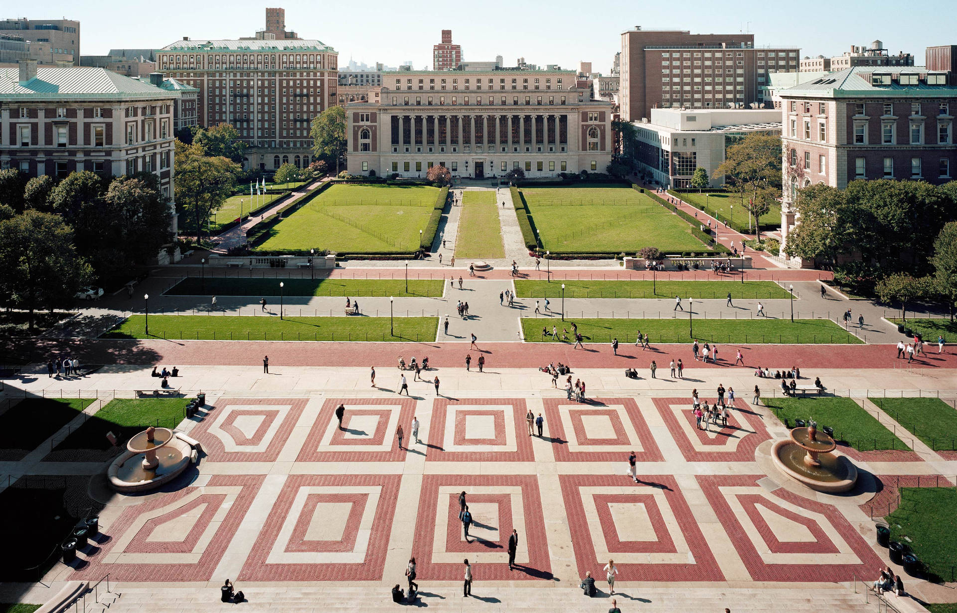 大學校園廣場，學生在紅磚圖案的地面上行走和坐著。