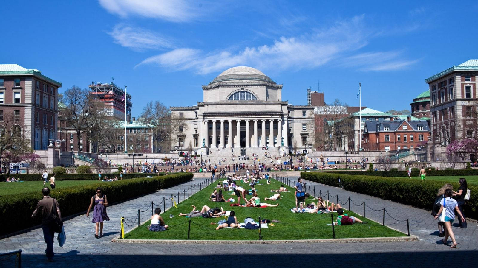 學生喺陽光普照嘅日子喺大學建築前面嘅草地上閒逛。