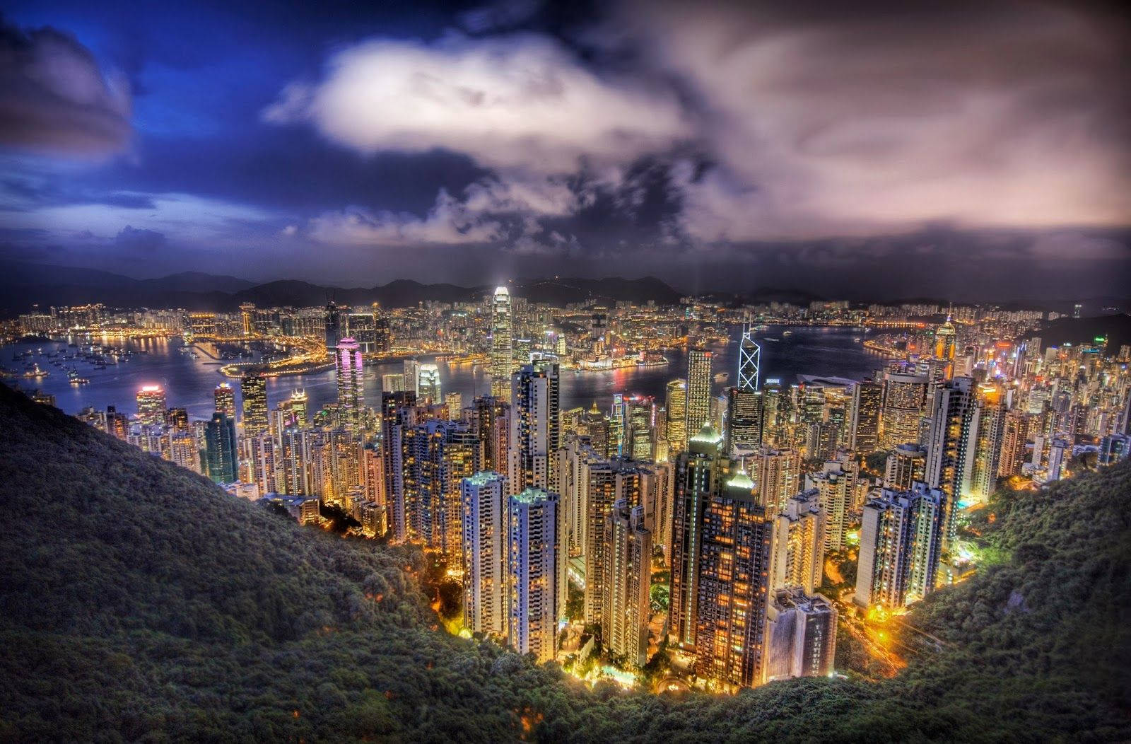 哥倫比亞波哥大 風暴夜 壁紙 — 香港令人驚嘆的夜景，摩天大樓在戲劇性的多雲天空下閃閃發光，坐落在鬱鬱蔥蔥的綠色山丘之間。