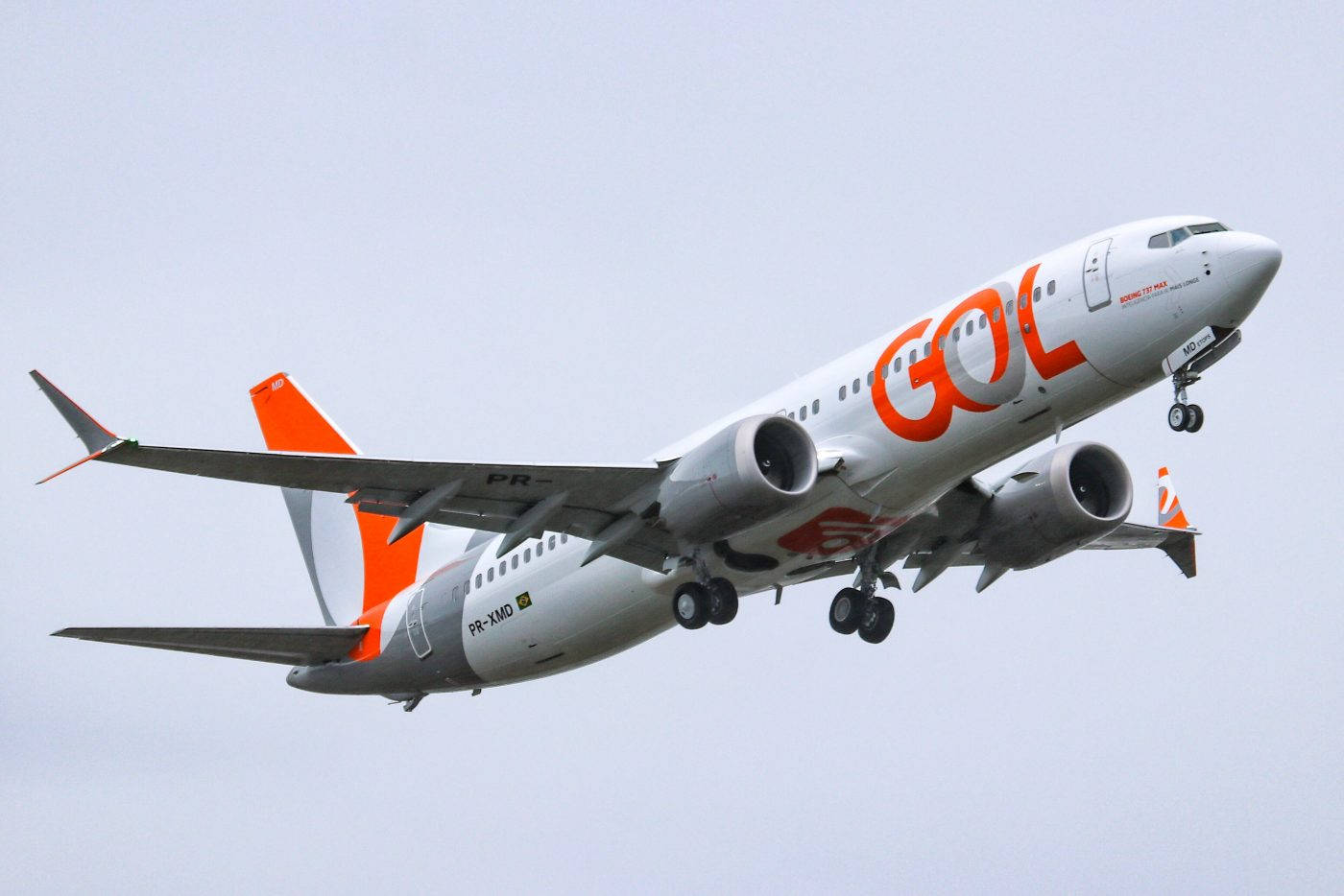 哥倫比亞航空飛機翱翔天際 壁紙 — 一架帶有橙色品牌標識的GOL航空波音737正在起飛，起落架放下，背景是淺灰色的天空。