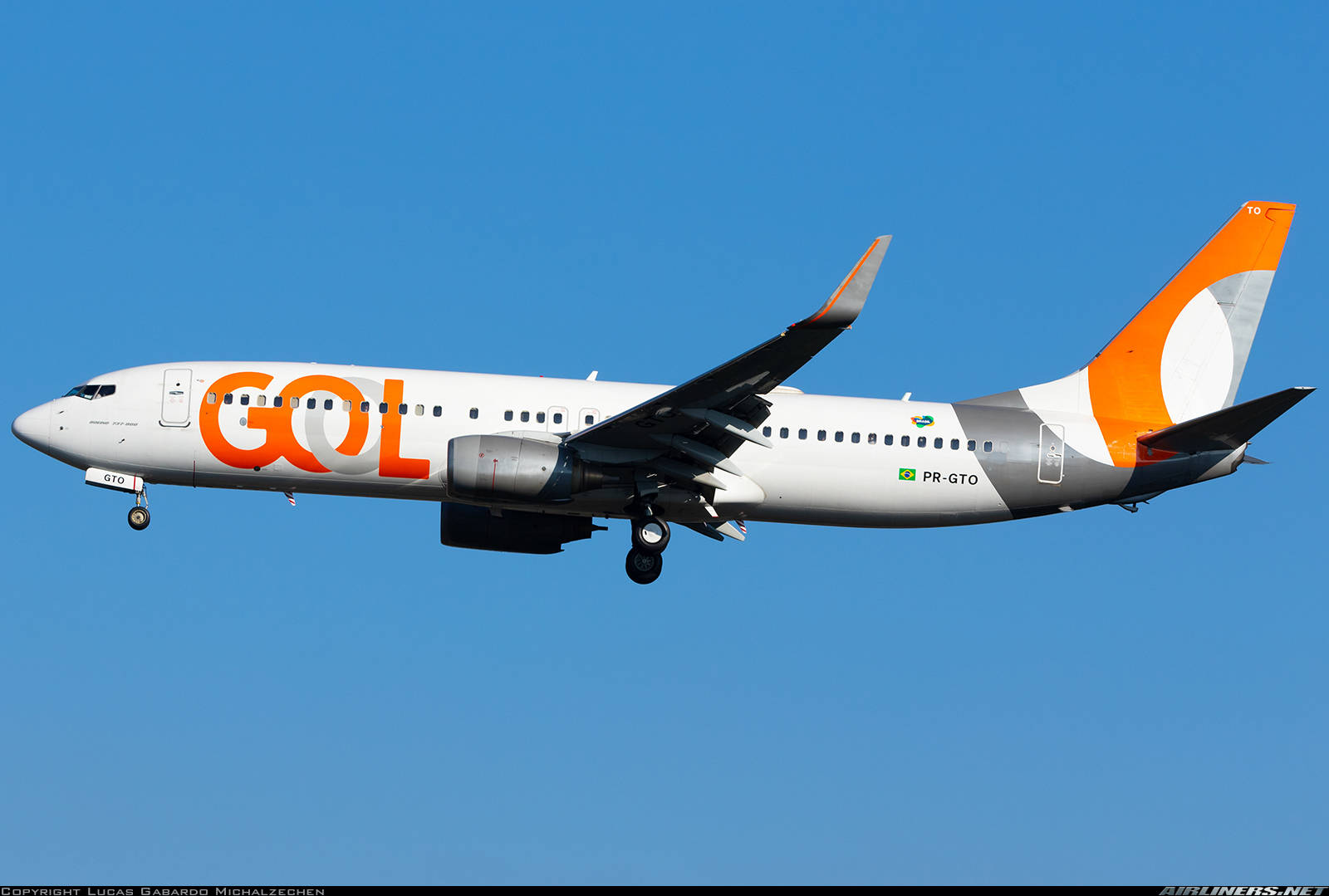 哥倫比亞航空飛機翱翔藍天 壁紙 — 一架GOL航空的波音737，白色和橙色塗裝，起落架放下，在清澈的藍天中飛行。