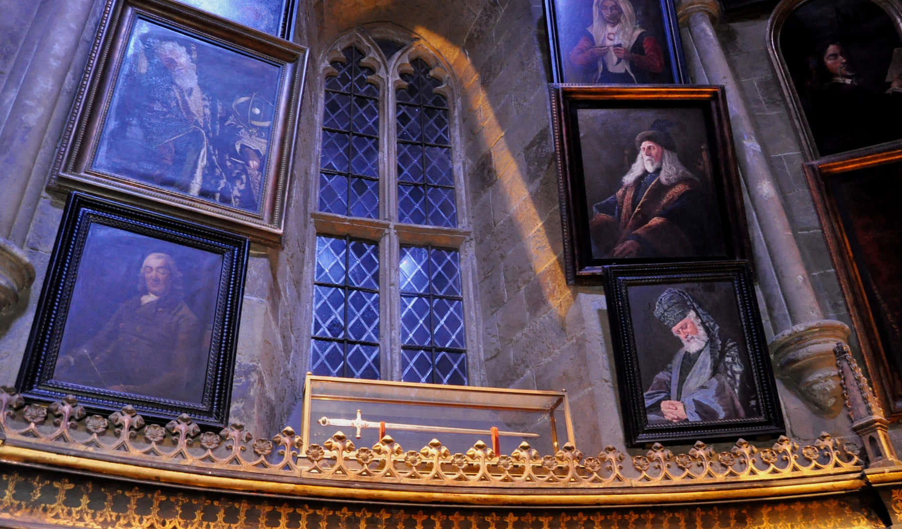 The Hogwarts Headmaster's Office 桌布 壁紙 — 哥德式石牆上裝飾著巫師的裱框肖像，鑽石窗格窗戶下方有一個劍盒。