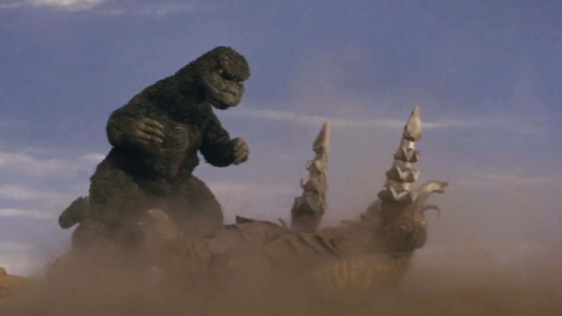 Godzilla Vs Megalon 桌布 壁紙 — 哥斯拉在晴朗藍天下，塵土飛揚的沙漠戰場上，勝利地站在被擊敗的怪物之上。