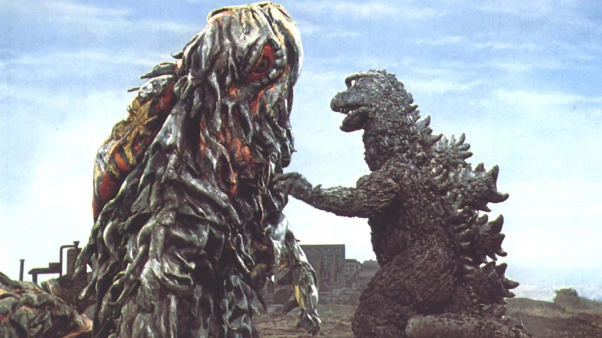 Godzilla Vs Hedorah 桌布 壁紙 — 哥斯拉在淡藍色天空下，於廢墟城市景觀中面對一個怪誕、融化的怪物。