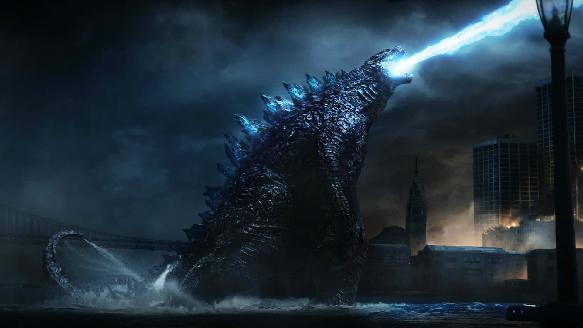 Godzilla City Destruction 桌布 壁紙 — 哥斯拉從黑暗城市景觀的水中出現，在暴風雨的天空下發射明亮的藍色原子吐息。