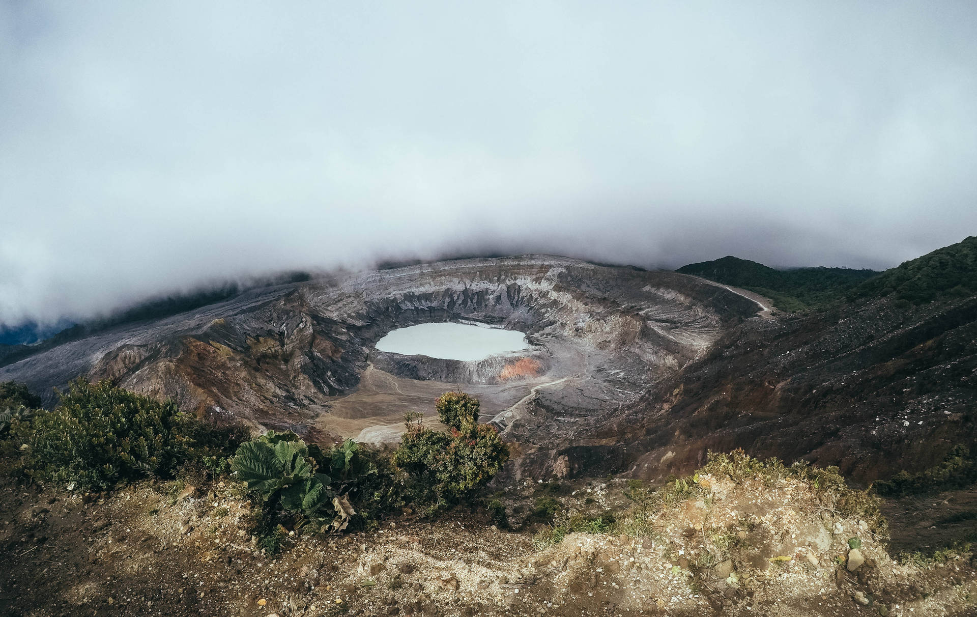火山口湖被霧氣和崎嶇地形環繞，有綠色植被。