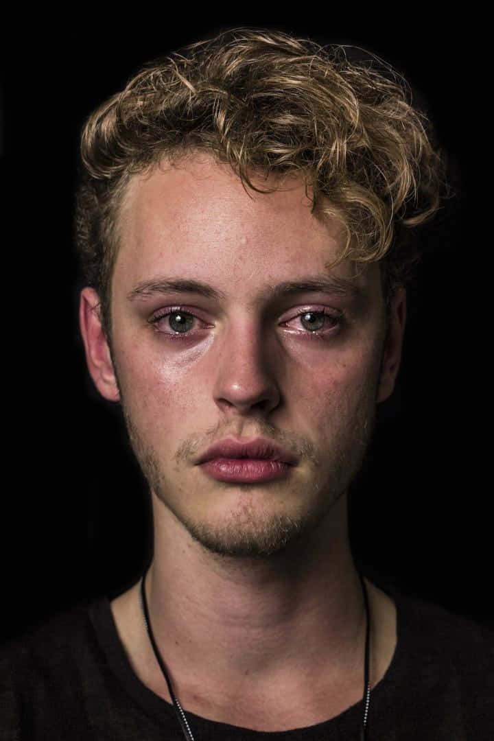 一個年輕男子，有著捲曲的金色頭髮和疲憊的眼睛的特寫肖像。