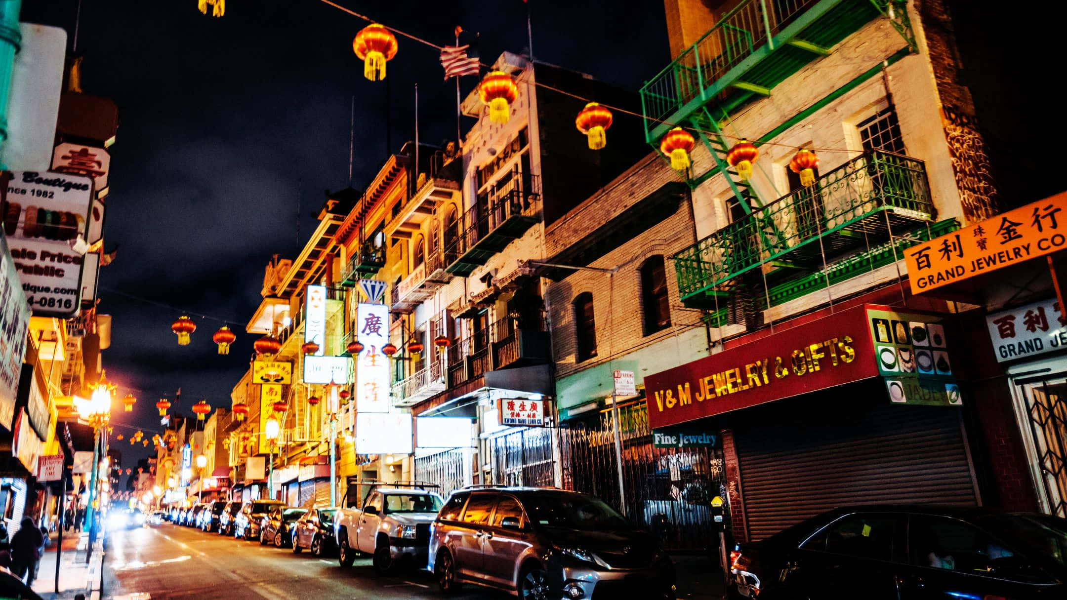 三藩市 桌布 壁紙 — 唐人街一條充滿活力的夜晚街道，被發光的紅燈籠和霓虹燈招牌照亮，倒映在停泊的汽車上。