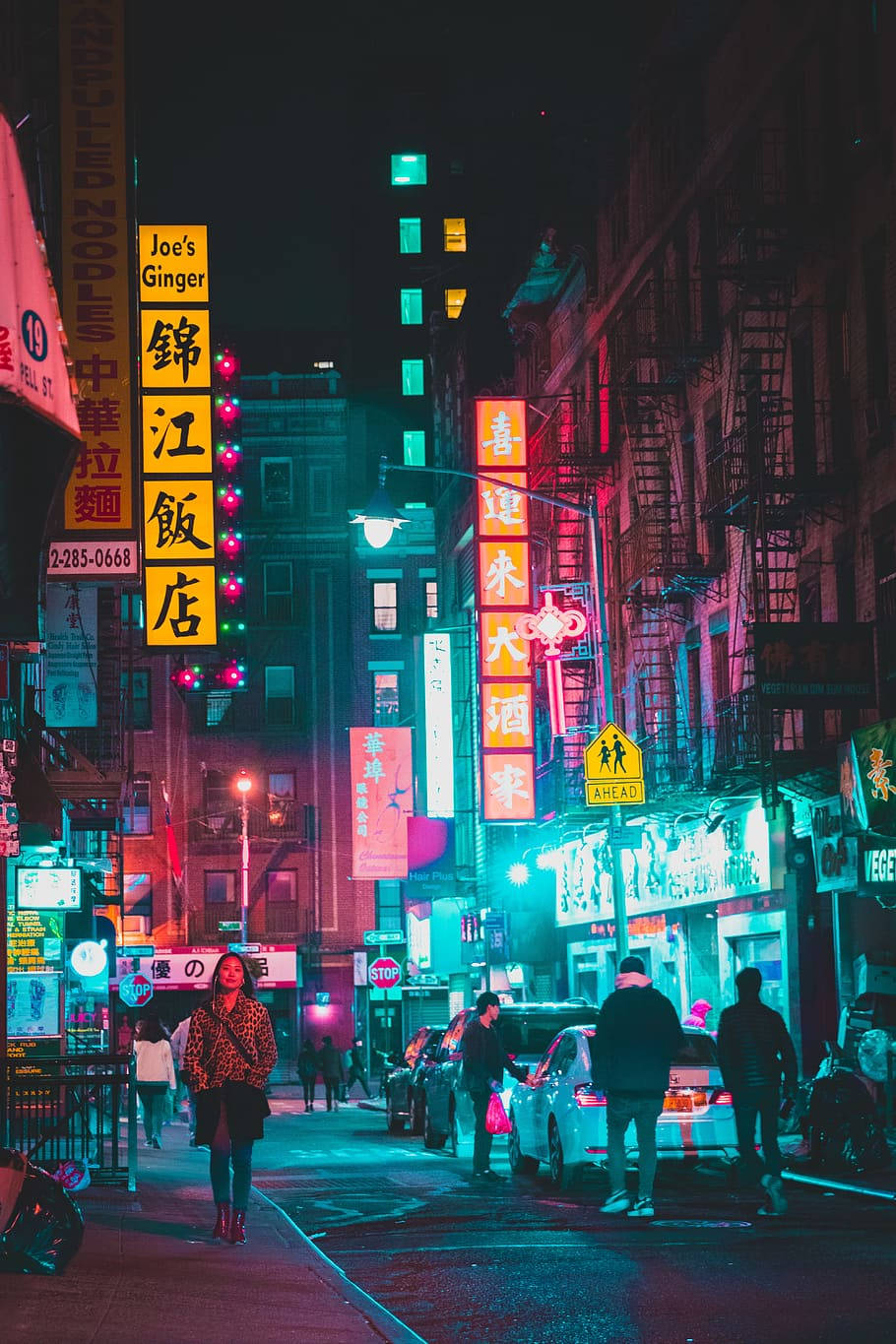 唐人街夜景霓虹燈 壁紙 — 充滿活力的霓虹燈牌在唐人街繁忙的夜間小巷中閃爍粉紅色和藍綠色，有行人和停泊的汽車。