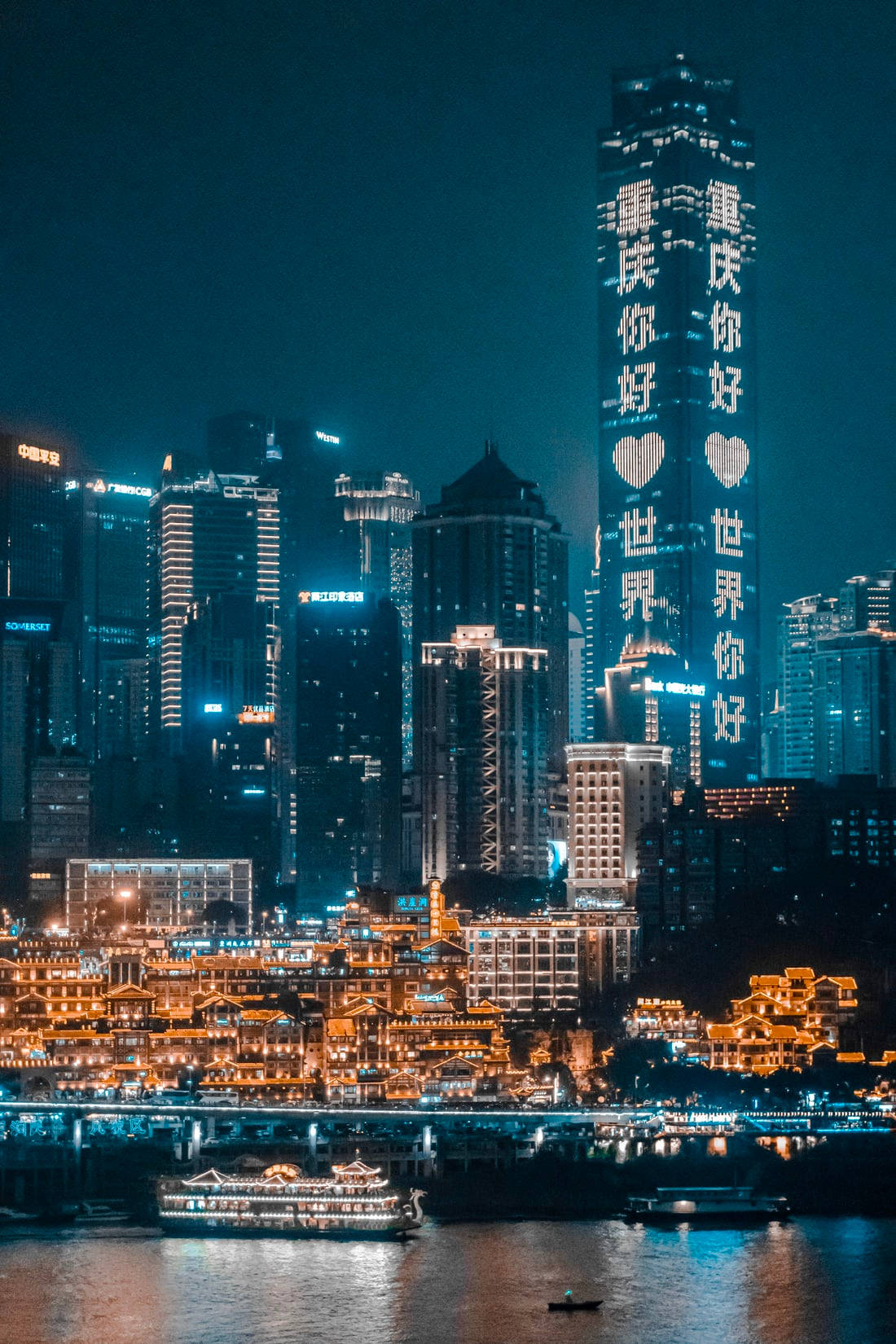 唐人街璀璨夜景 壁紙 — 充滿活力的夜景，河邊有燈火通明的摩天大樓和傳統建築，還有船隻。