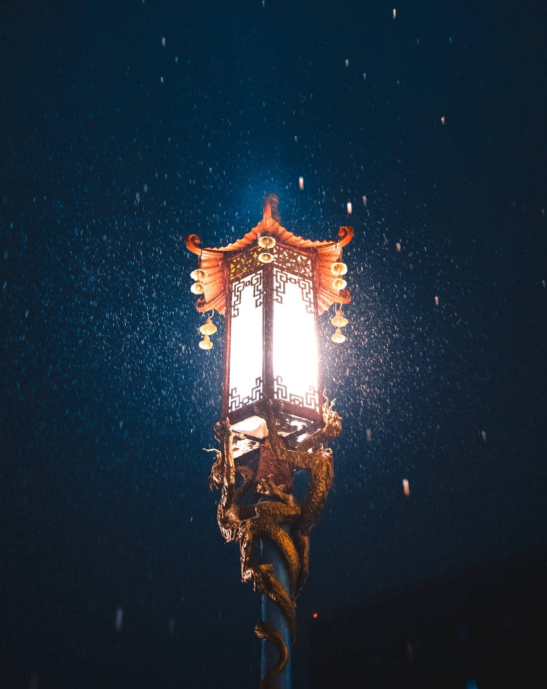 唐人街街燈雪夜 壁紙 — 一個帶有龍紋的傳統發光燈籠，在黑暗的雪夜天空中溫暖地閃耀。