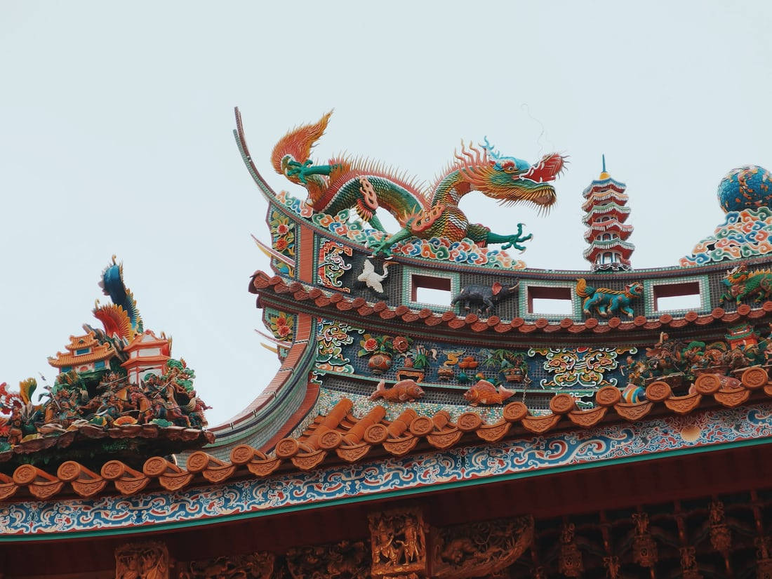 唐人街龍神雕像 壁紙 — 色彩鮮豔、裝飾華麗的龍雕塑，在淡色天空的襯托下，矗立在傳統瓦片屋頂之上。