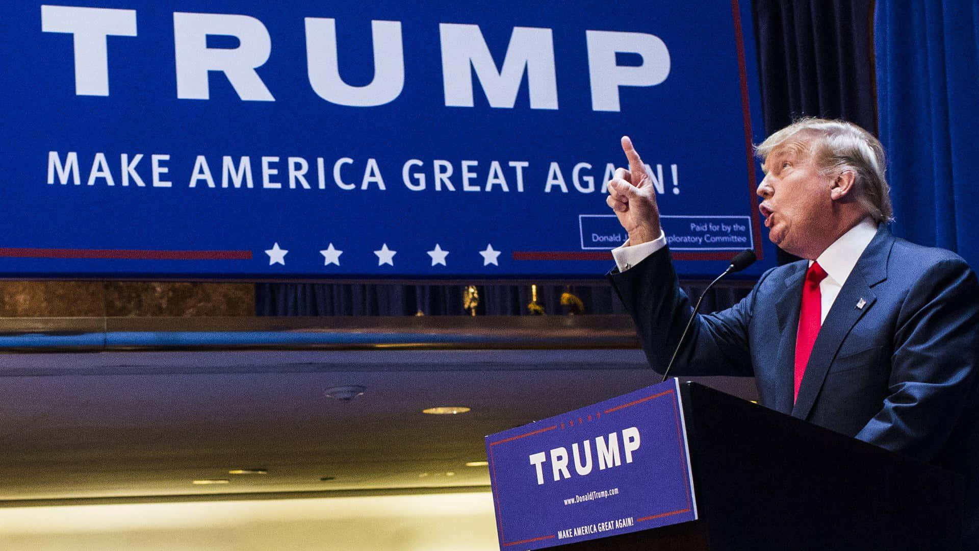 trump 桌布 壁紙 — 唐納德·特朗普在一個大型藍色「TRUMP MAKE AMERICA GREAT AGAIN」橫幅下的講台上，一邊說話一邊用力做手勢。