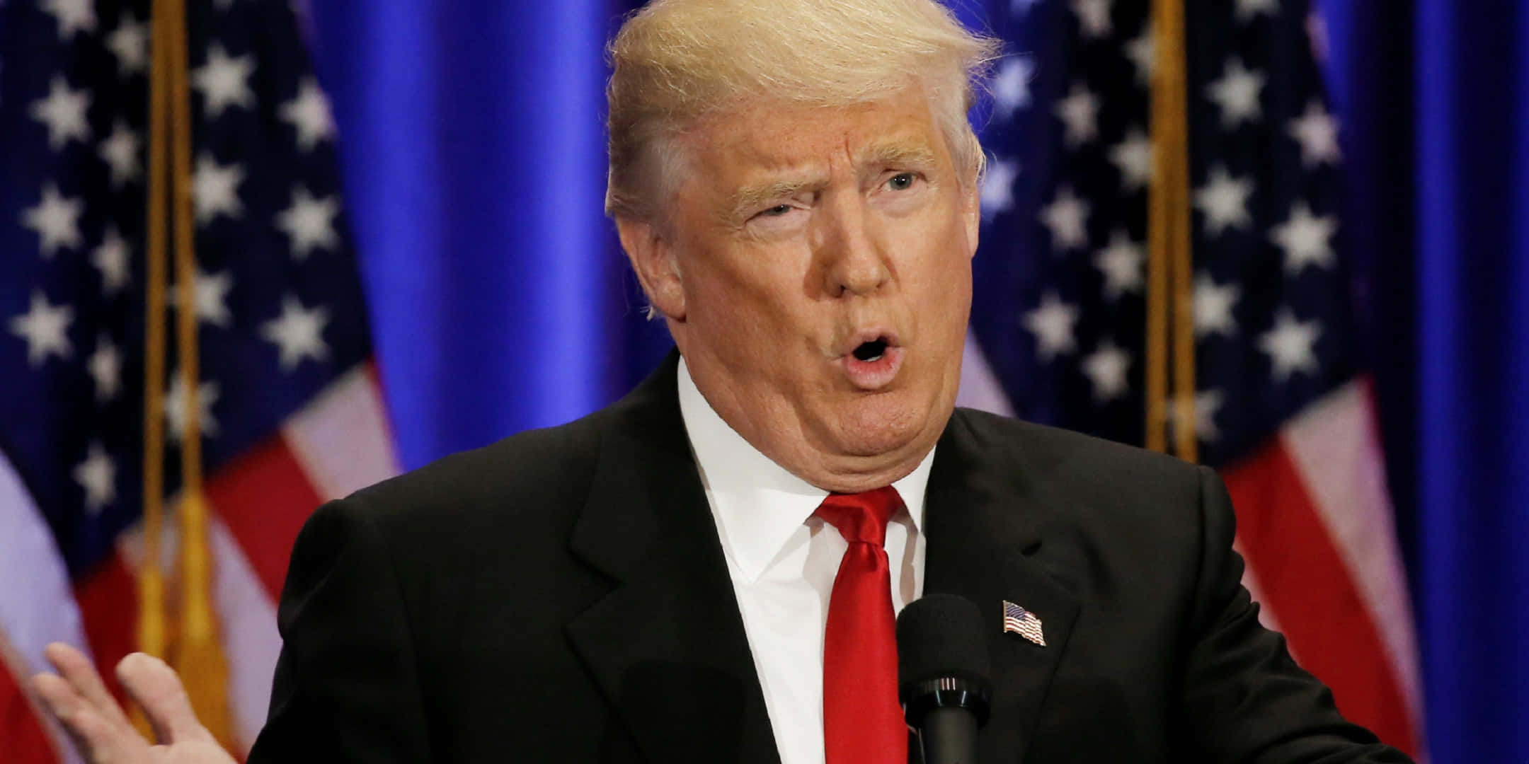 trump 桌布 壁紙 — 唐納德·特朗普在正式場合中，身後有美國國旗，在講台上充滿激情地演講。