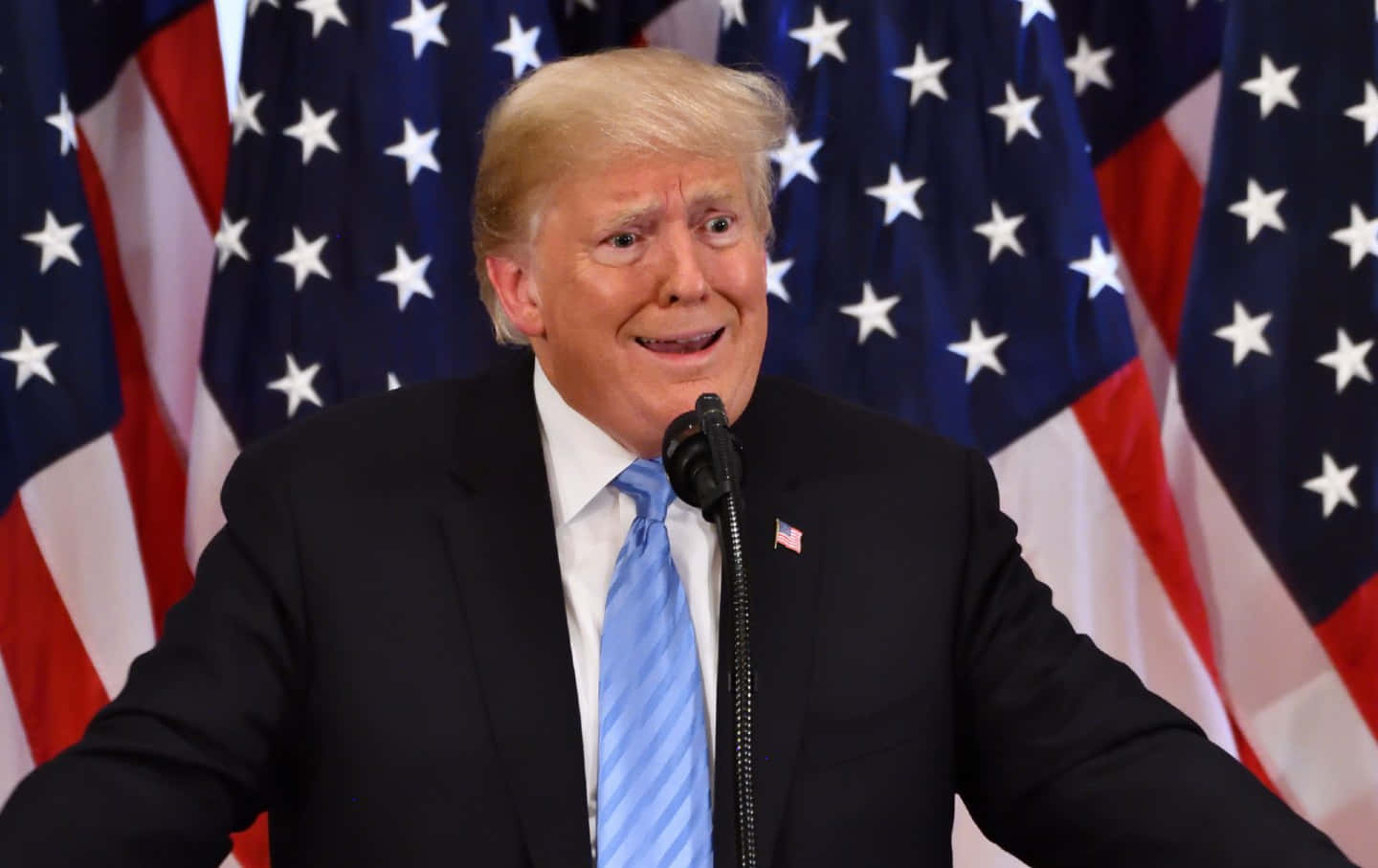 trump 桌布 壁紙 — 唐納德·特朗普在美國國旗前對著麥克風說話，露出燦爛的笑容。