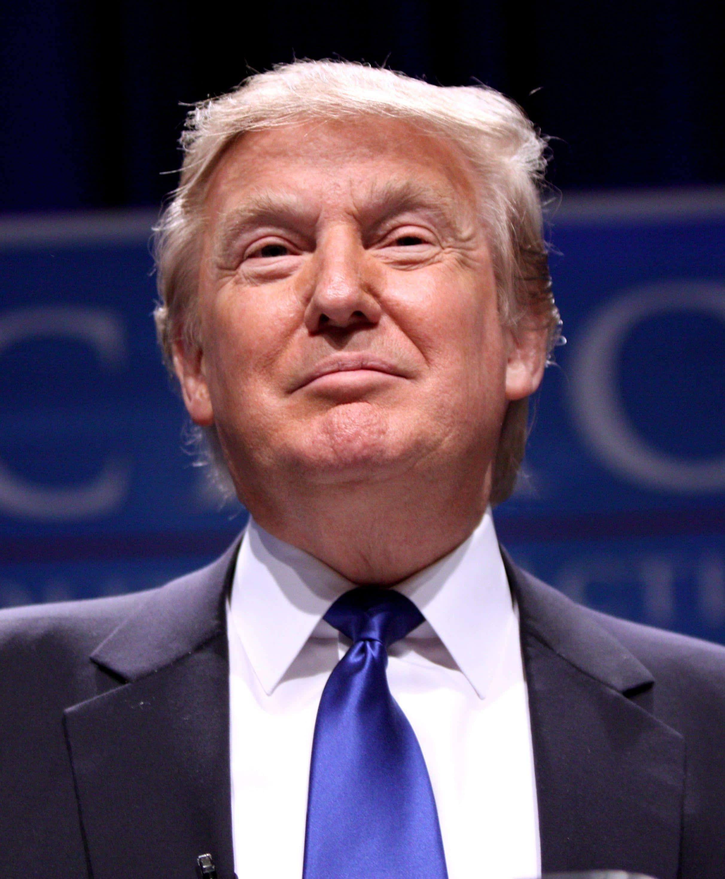 trump 桌布 壁紙 — 唐納德·特朗普的近距離肖像，身穿深色西裝和藍色領帶，背景為模糊的藍色。