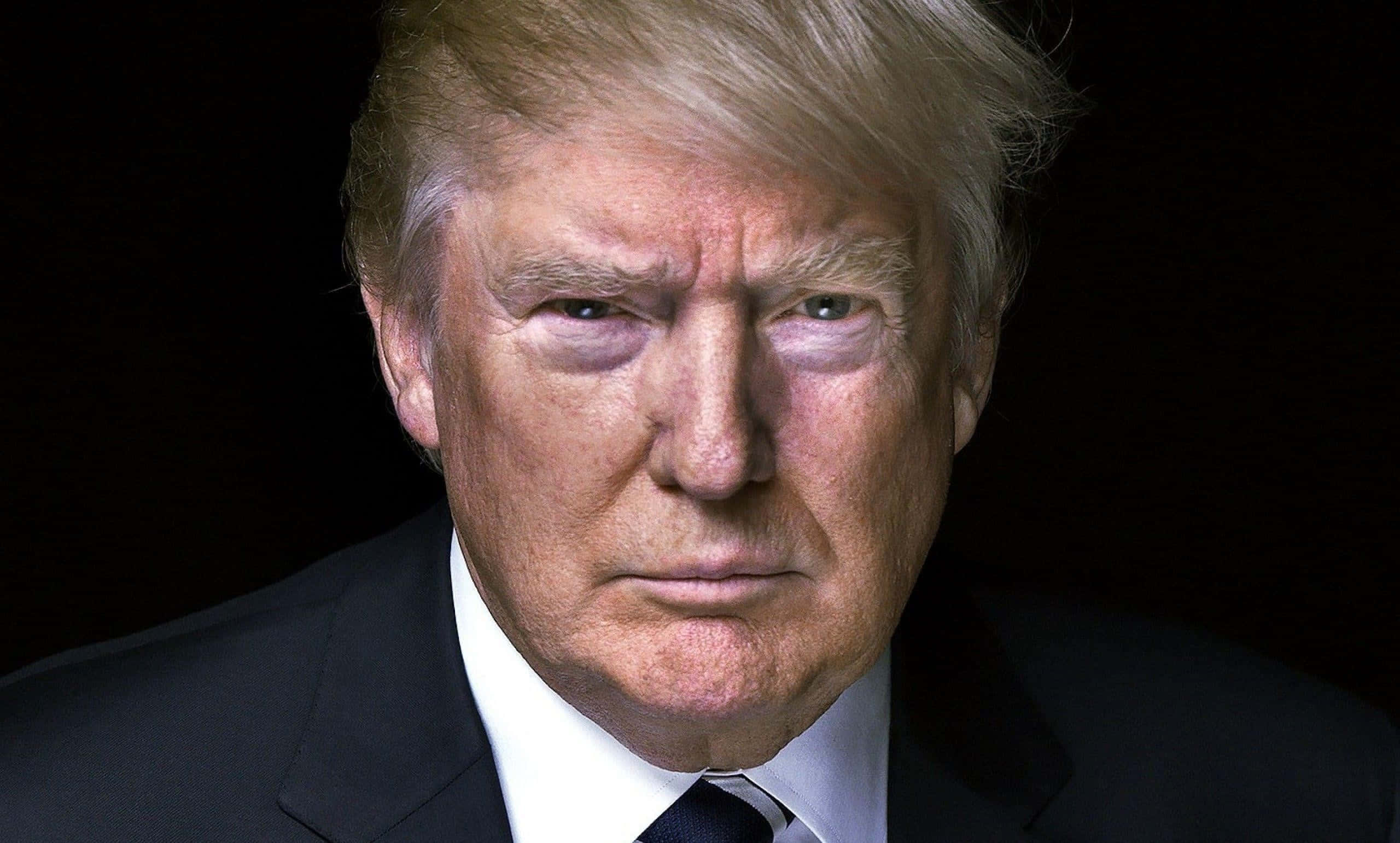 trump 桌布 壁紙 — 唐納德·特朗普身穿深色西裝，在黑色背景前的特寫肖像，眼神直接而強烈。