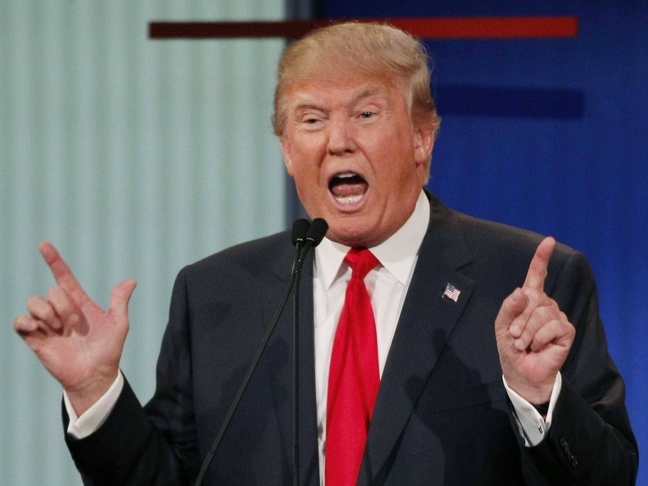 donald trump 桌布 壁紙 — 唐納德·特朗普身穿深色西裝和紅色領帶，在政治活動中對著麥克風說話時，做出強調的手勢。