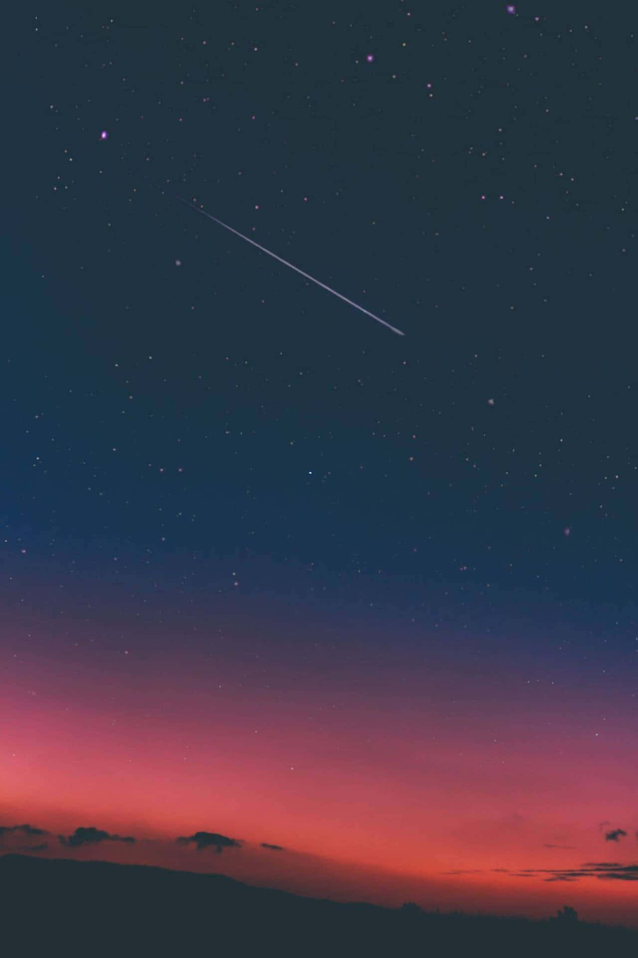 一顆流星劃過黑暗山丘上方佈滿星星的暮色天空。