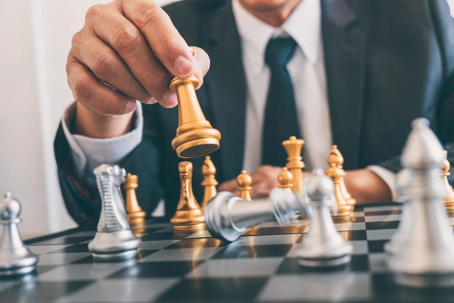 商務人士下棋謀略 壁紙 — 一位身穿西裝的商人正在棋盤上移動一枚金色棋子，銀色棋子清晰對焦。