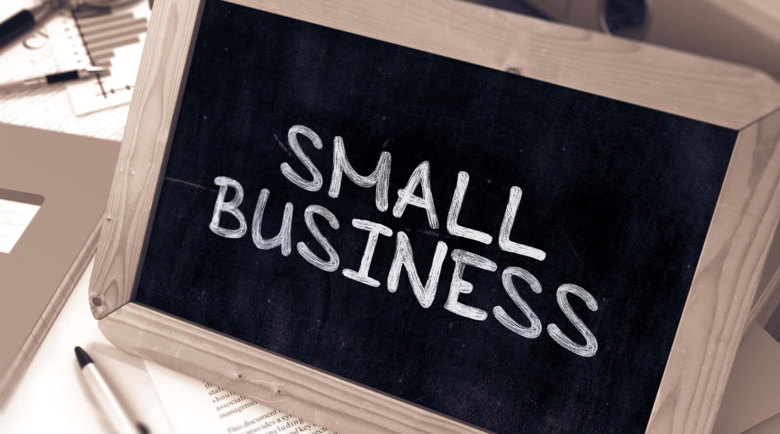 黑板，上面用白色粉筆寫著small business，放在有辦公用品的桌子上。